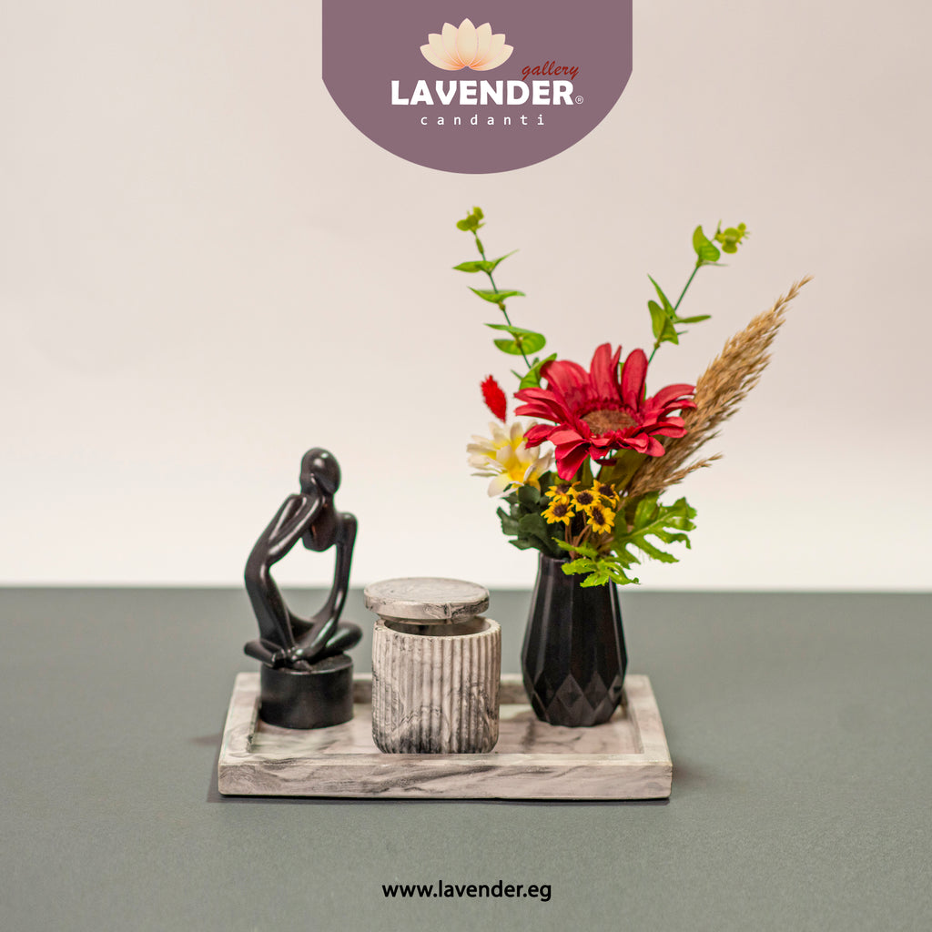 Decorative setup with a statue, candle, and vase of flowers on a marble tray, 