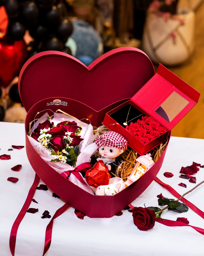 Heart-shaped gift box with a doll and flowers on a white surface