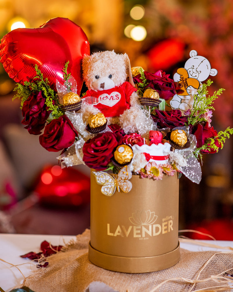 Decorative flower arrangement with a teddy bear, heart-shaped balloon, and 'LAVENDER' branding.