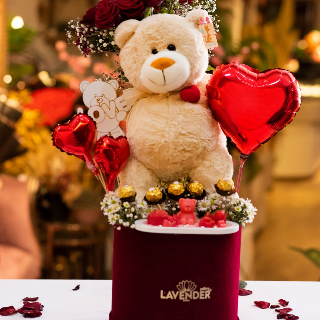 Teddy bear with red roses, heart balloons, and small teddy bears in a decorative box labeled 'Lavender'.