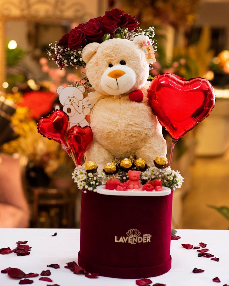 Teddy bear with red roses, heart balloons, and small teddy bears in a decorative box labeled 'Lavender'.