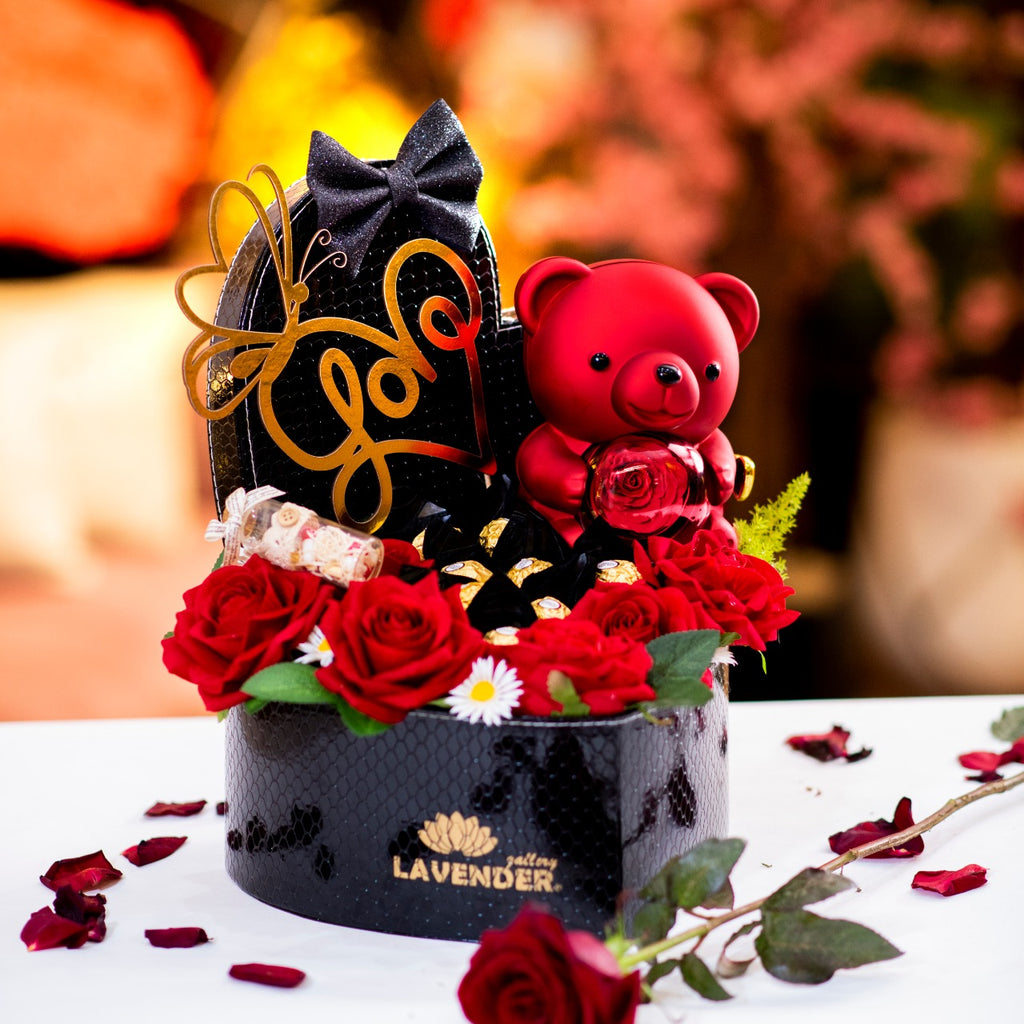 Decorative arrangement with a black cat, red teddy bear, and flowers on a white surface.